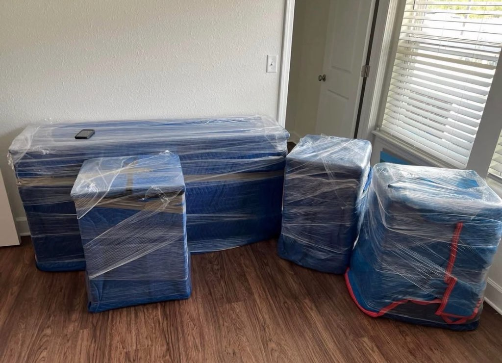 Furniture wrapped in blue plastic and secured with red straps in an empty room